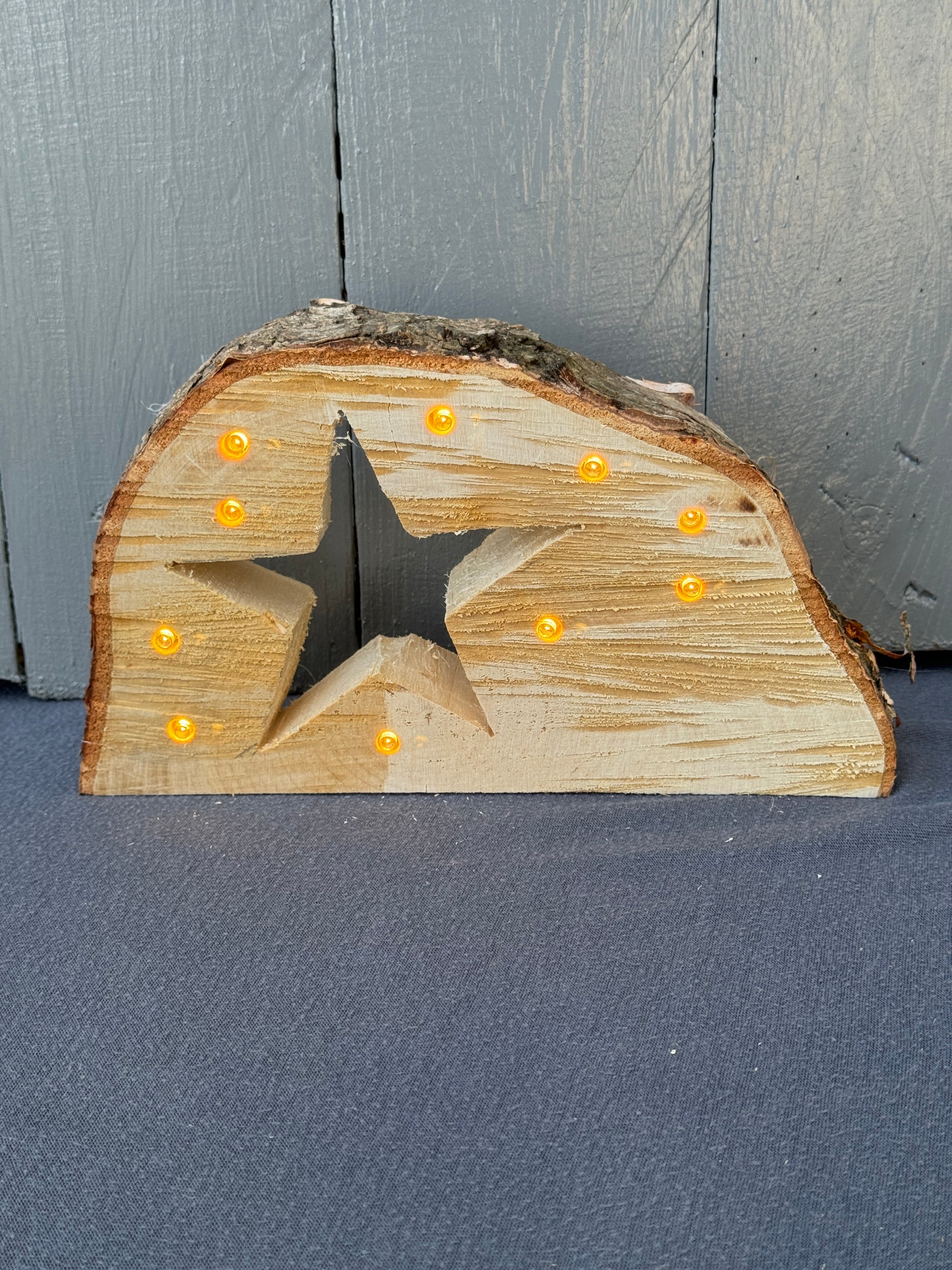 Handgefertigte Baumscheibe aus naturbelassenem Holz mit eingesägtem Stern und integrierter LED-Lichterkette – warmweiß leuchtend.