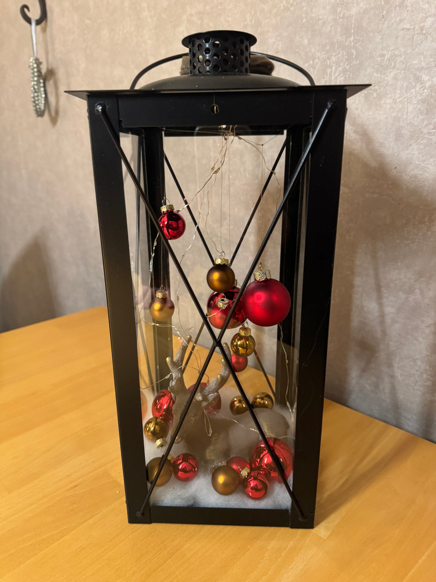 Nahaufnahme der handdekorierten Weihnachtslaterne – Hirsch im Kunstschnee mit funkelnden Lichtern und gläsernem Laternengehäuse.