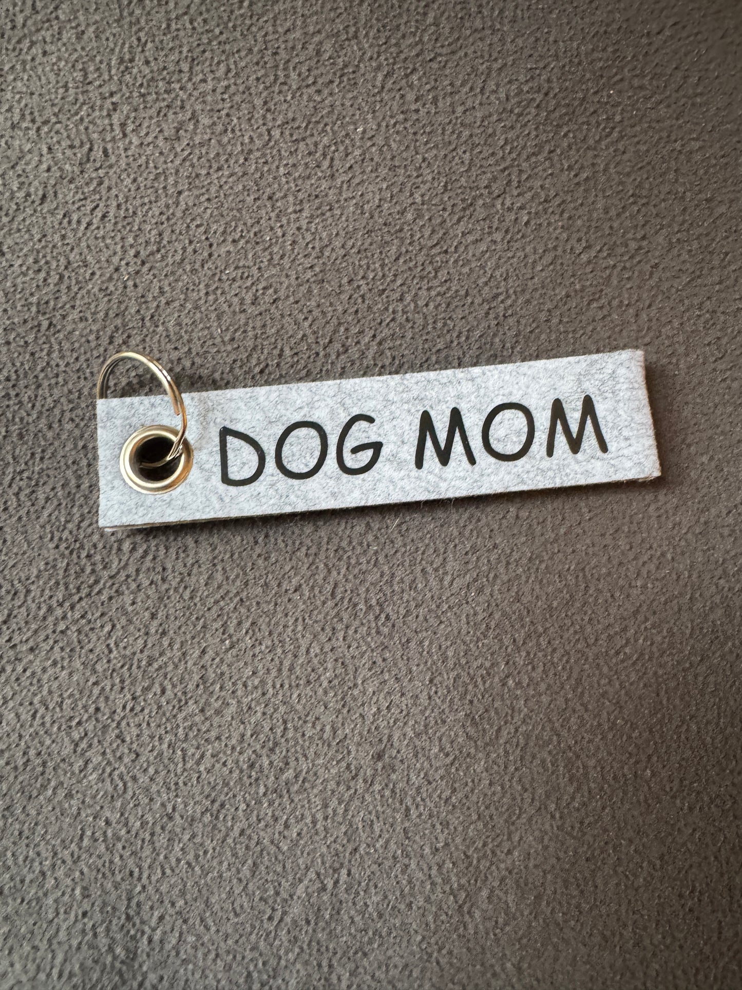 Grauer Filz-Schlüsselanhänger mit der Aufschrift „DOG MOM“.