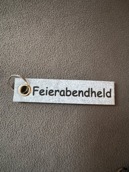 Schlüsselanhänger aus Filz mit dem Motiv „Feierabendheld“ in Grau.