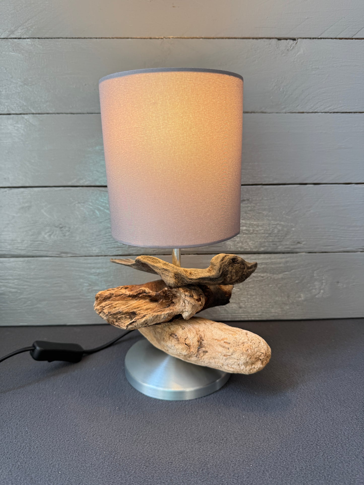 Nachhaltige Tischlampe aus Ostsee-Treibholz mit runder Metallbasis.