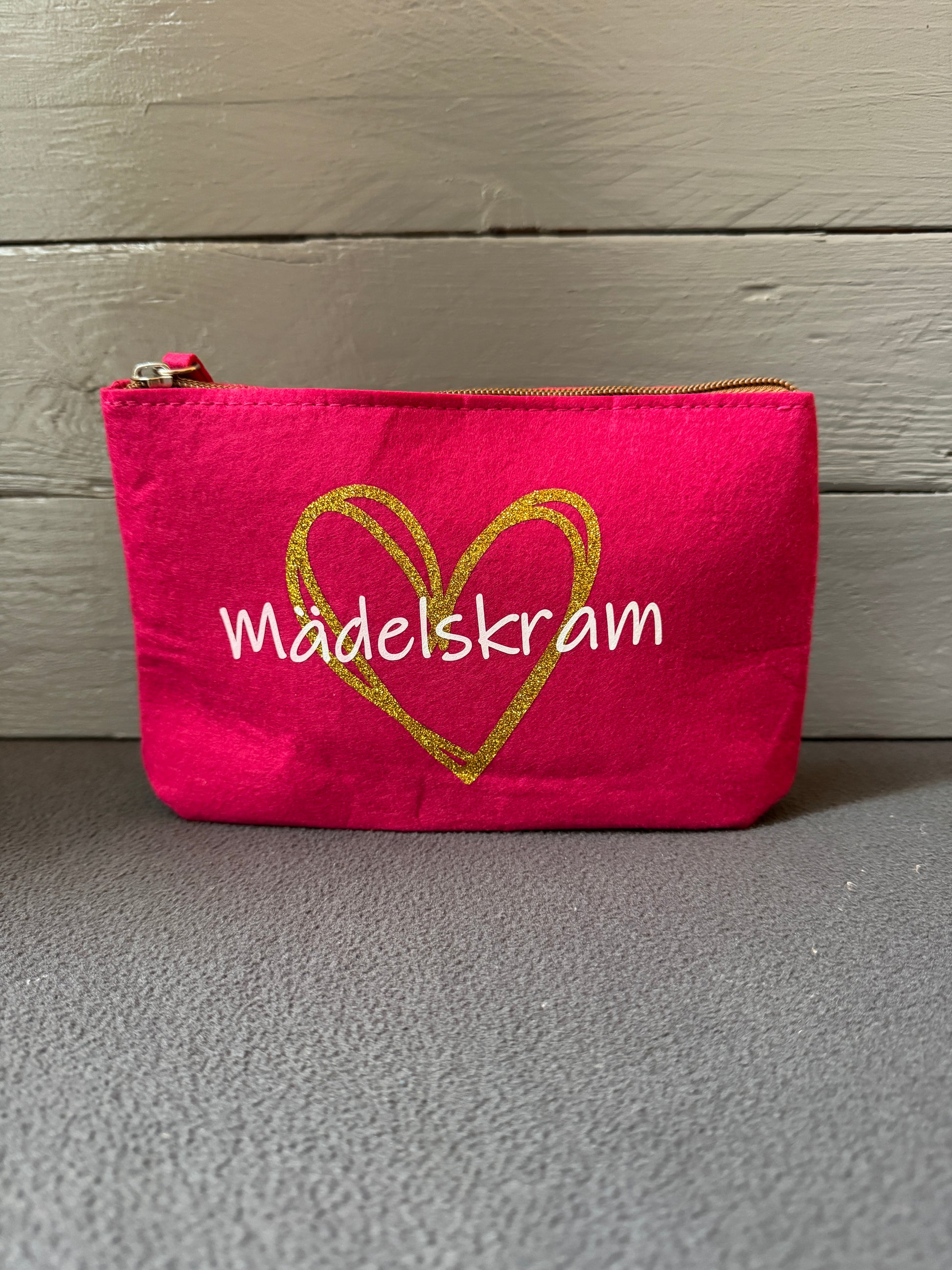 Kosmetiktasche aus Filz in Pink mit goldenem Herz und Schriftzug „Mädelskram“.