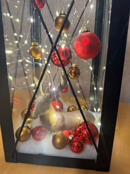 Weihnachtslaterne mit Hirschfigur, gold-roten Kugeln und warm leuchtender Lichterkette – handgefertigte Dekoration für die Adventszeit.