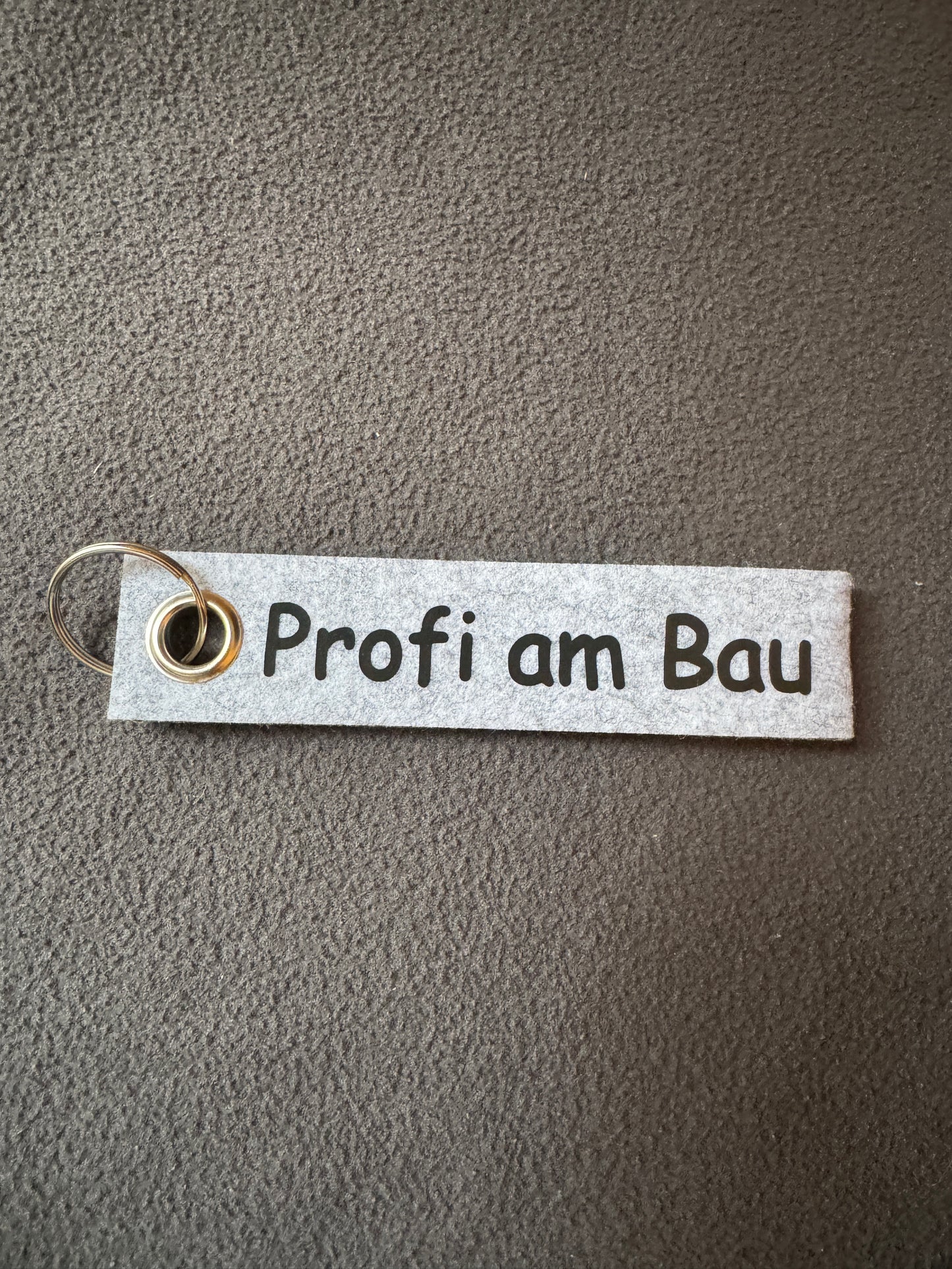 Grauer Filzanhänger mit dem Schriftzug „Profi am Bau“.