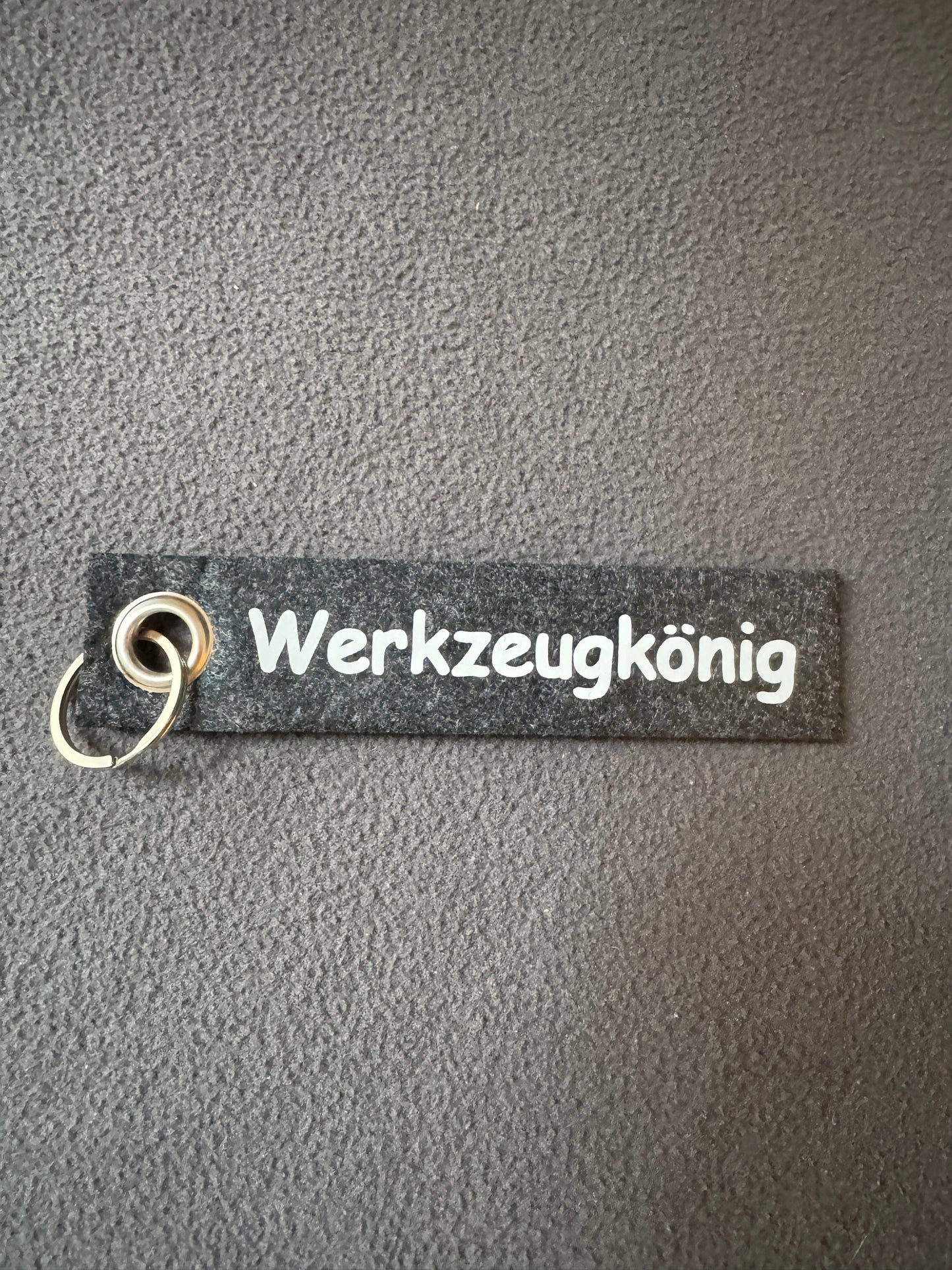 Grauer Filz-Schlüsselanhänger mit dem Text „Werkzeugkönig“.
