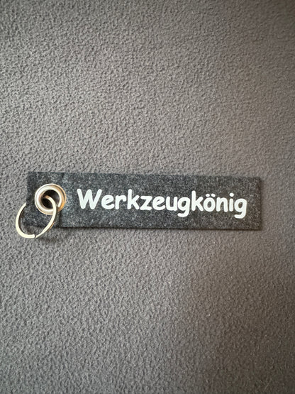 Grauer Filz-Schlüsselanhänger mit dem Text „Werkzeugkönig“.