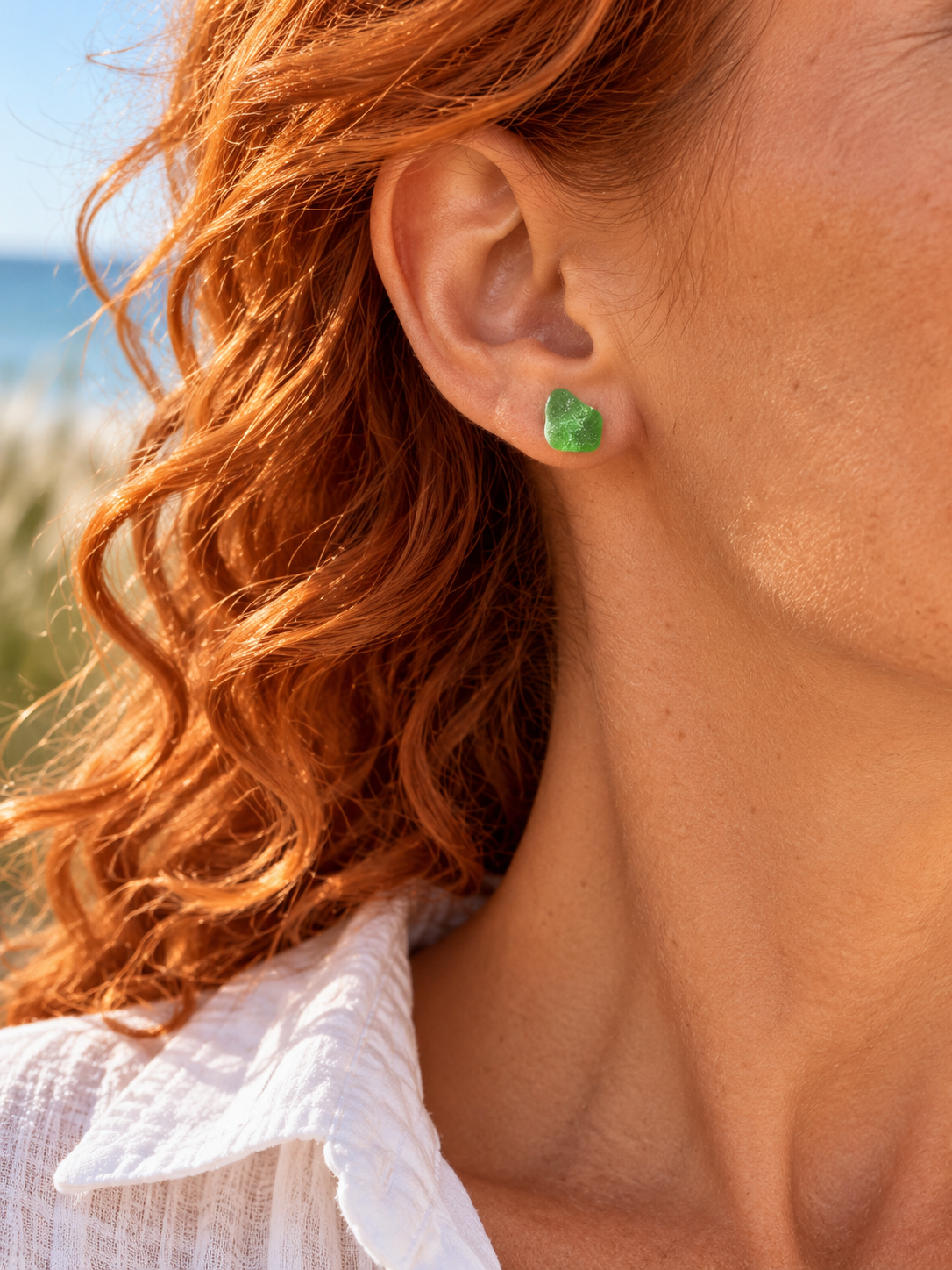 Grüner Meerglas-Ohrstecker mit ca. 1 cm Größe am Ohr einer Frau mit roten Locken