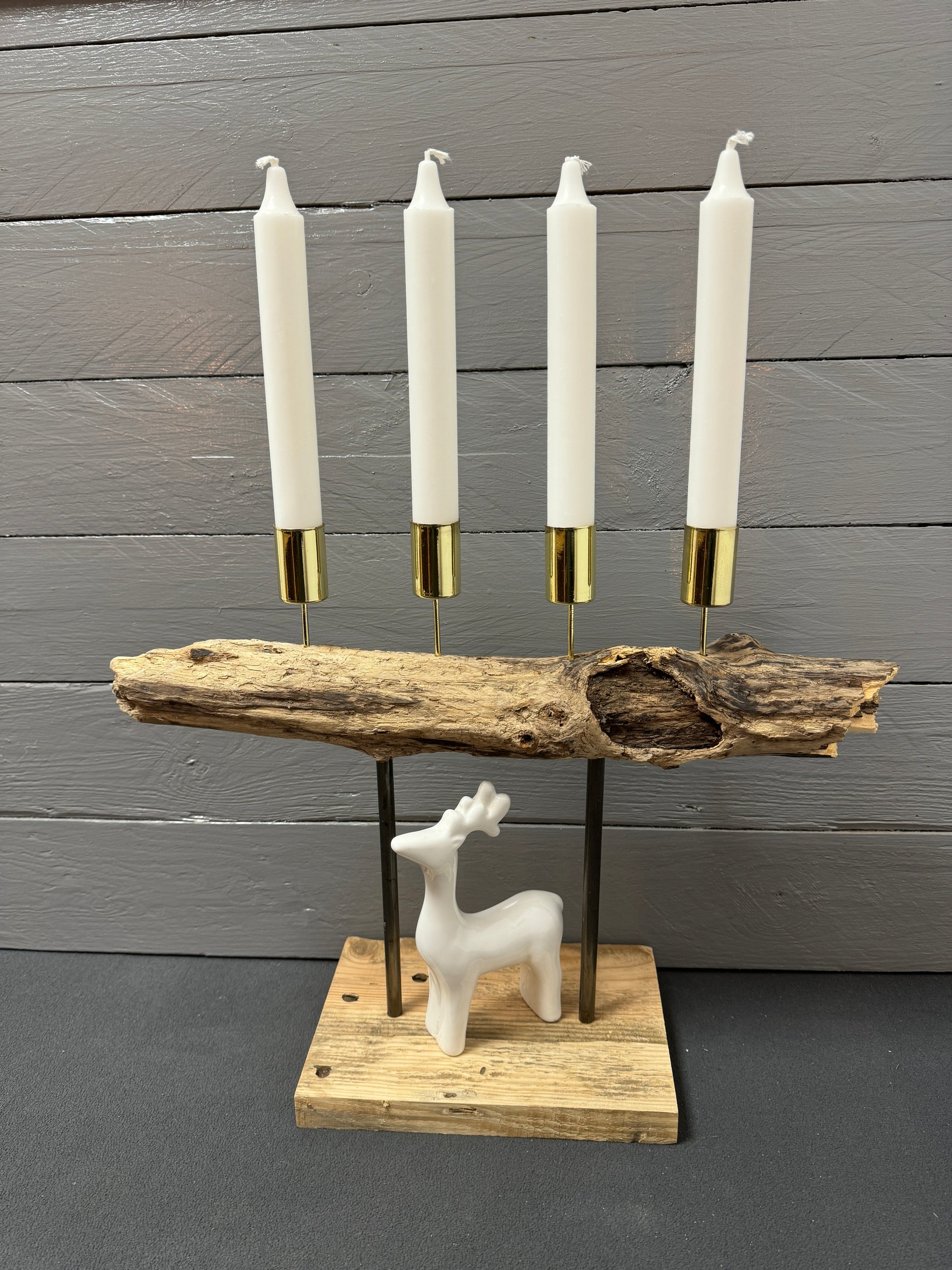 Handgefertigtes Treibholz-Adventsgesteck „Adventsfeuer Goldküste“ mit vier goldenen Stabkerzenhaltern auf geflammtem Holz – Vorderansicht.
