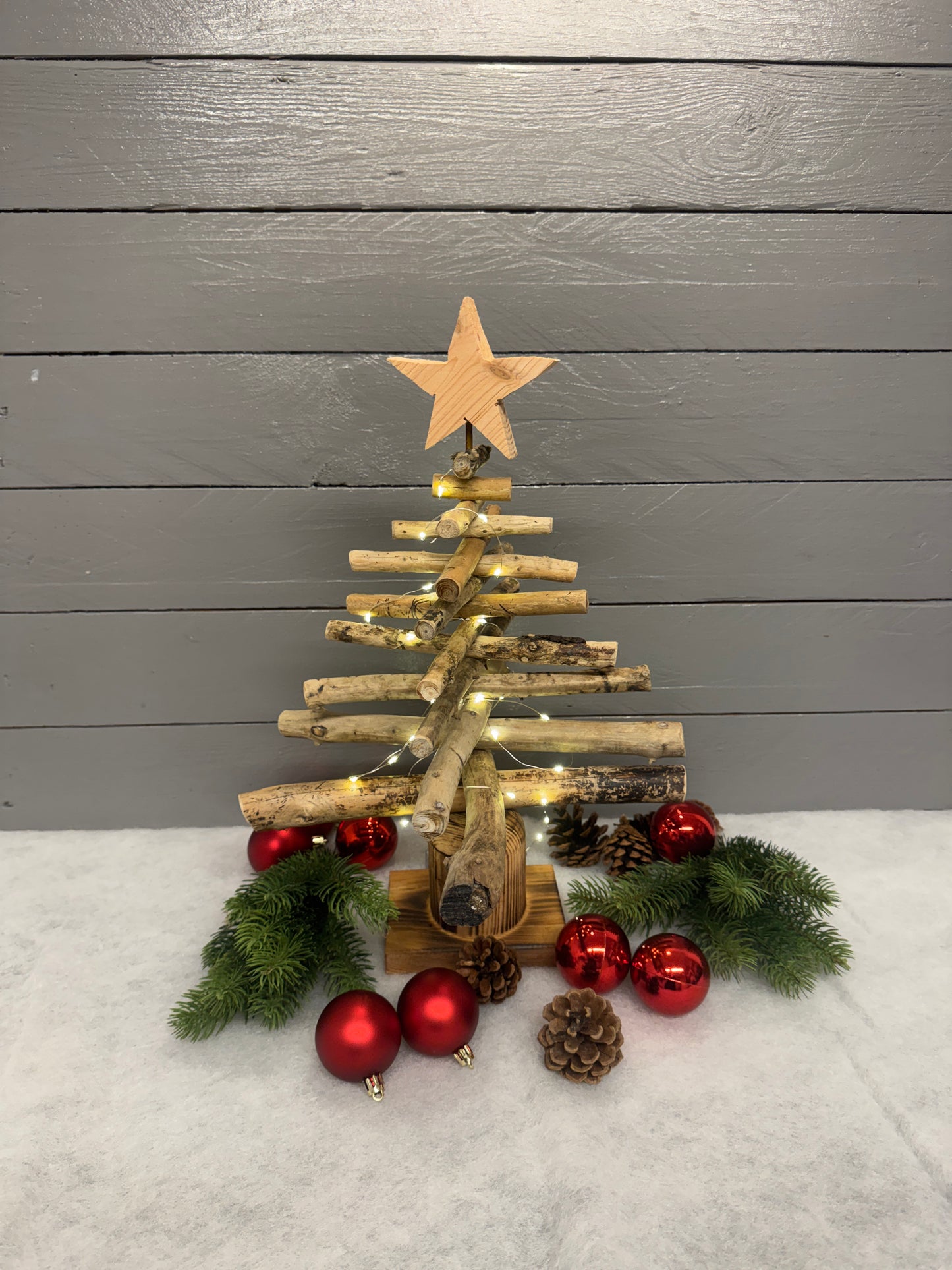 Detailaufnahme des geflammten Altholzfußes und der natürlichen Treibholzäste des handgefertigten Weihnachtsbaums.